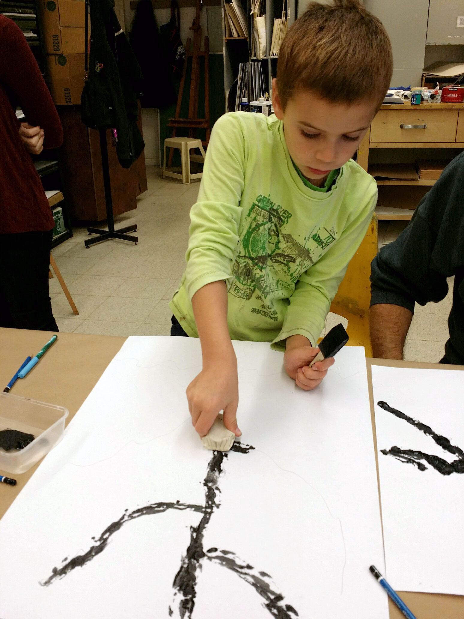Child painting a large tree design with black paint on white paper.