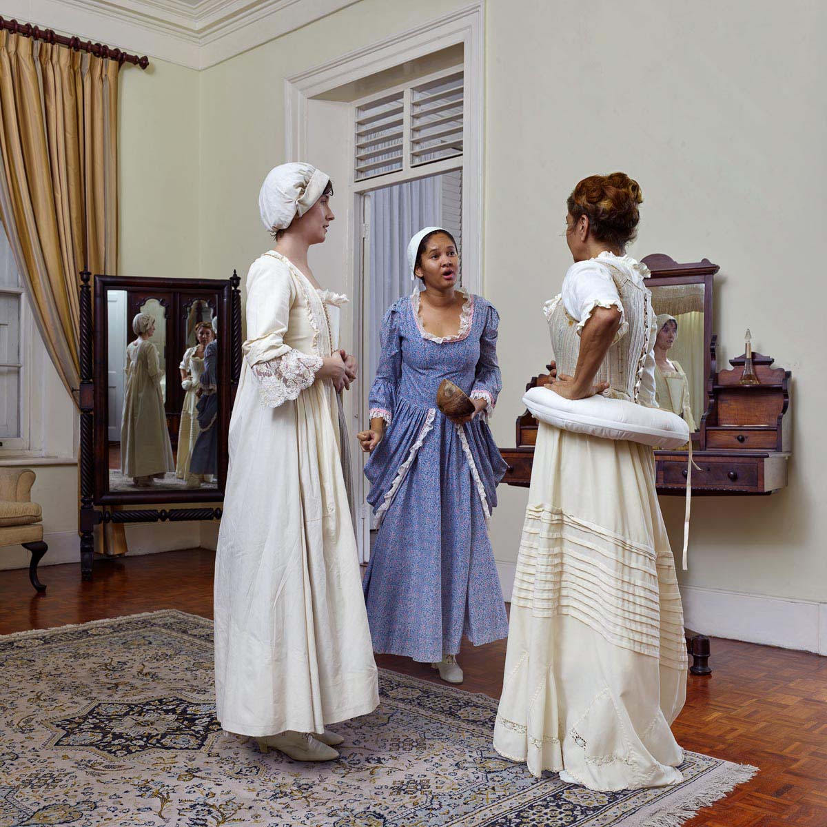 Three figures in historical attire appear to have an argument inside professionally lit luxurious room