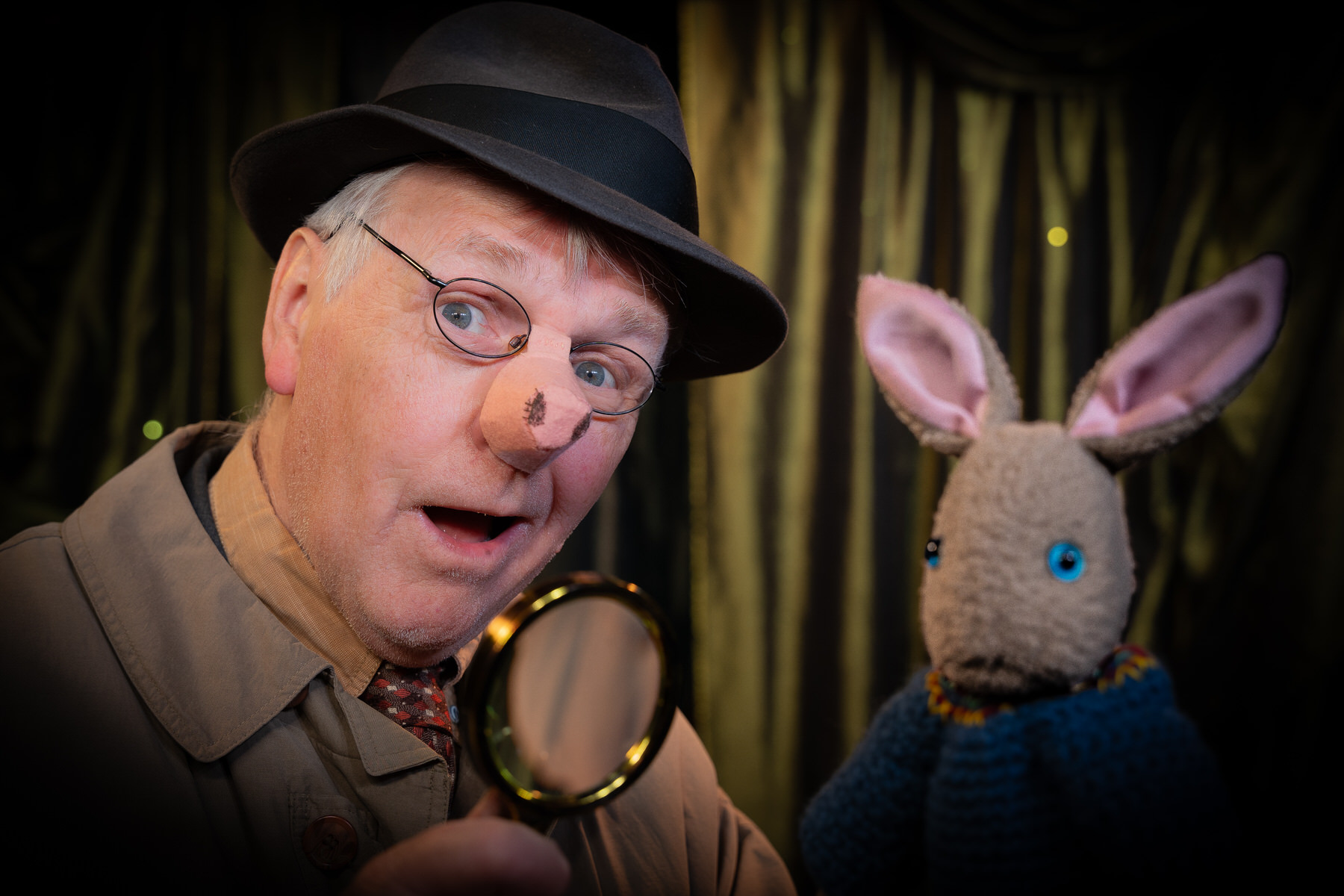 Detective-style figure holding a magnifying glass beside a knitted rabbit puppet.