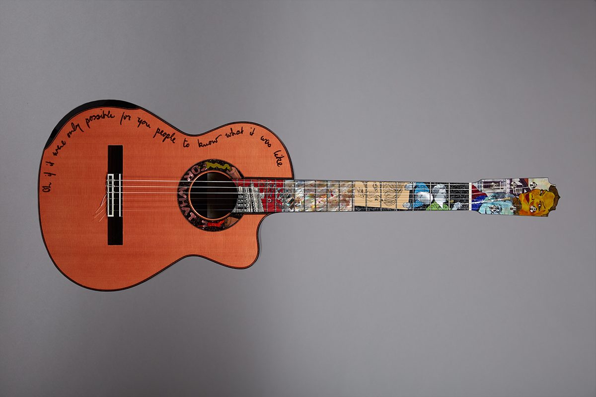 photograph of guitar with detailed inlay on fingerboard and writing around the edge of top half of the body