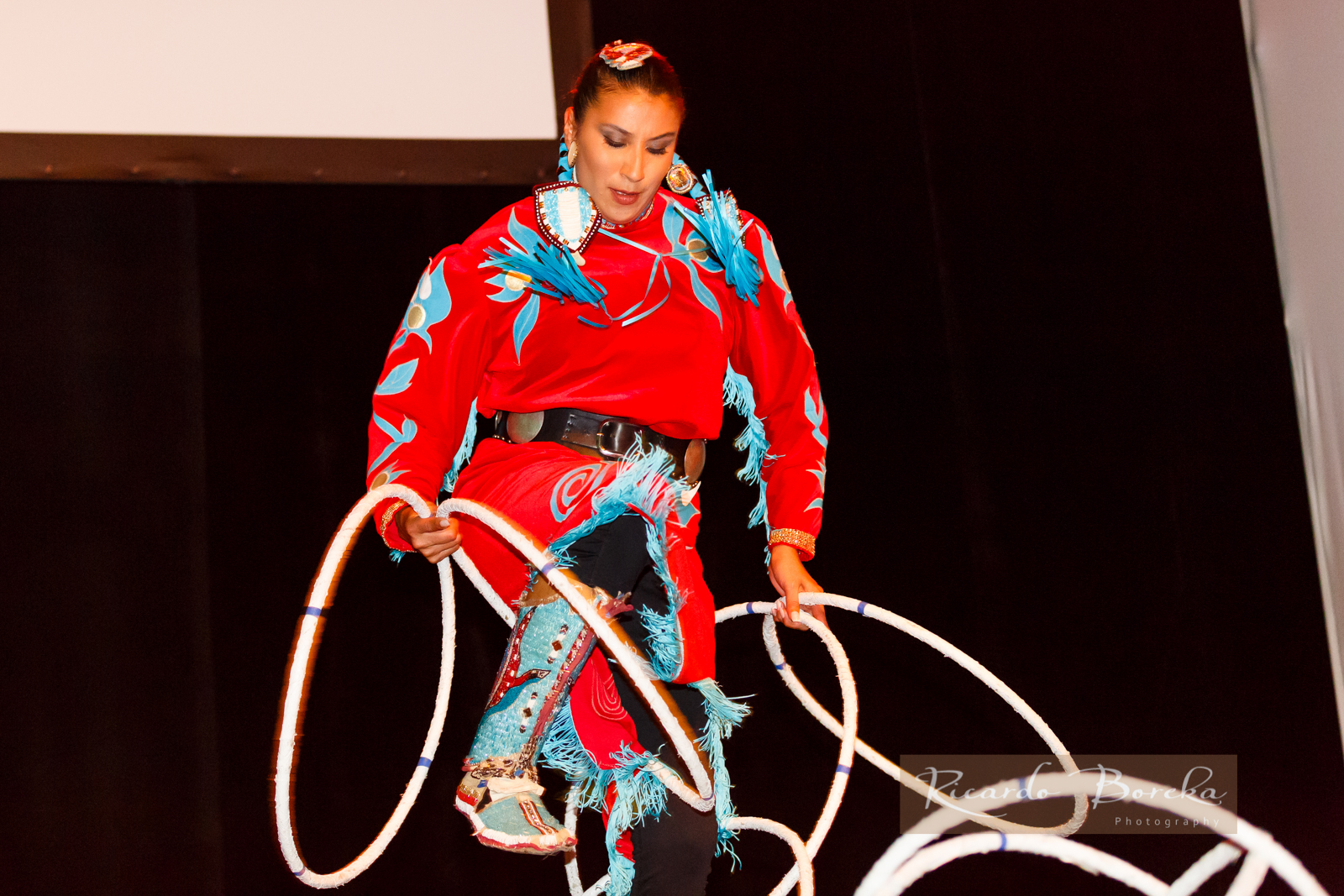 photograph of first nations woman dancing with hoops, wearing a red and blue costume