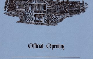 Image of the cover of the programme of the official opening of the McMIchael Canadian Art Collection. Image of log and stone building with trees at each side. The cover is blue with black printing.