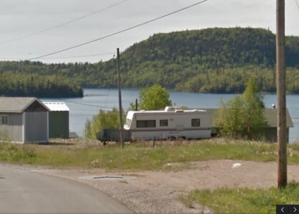 photograph of a trailer and small buildings with lake and wooded hillsides in background