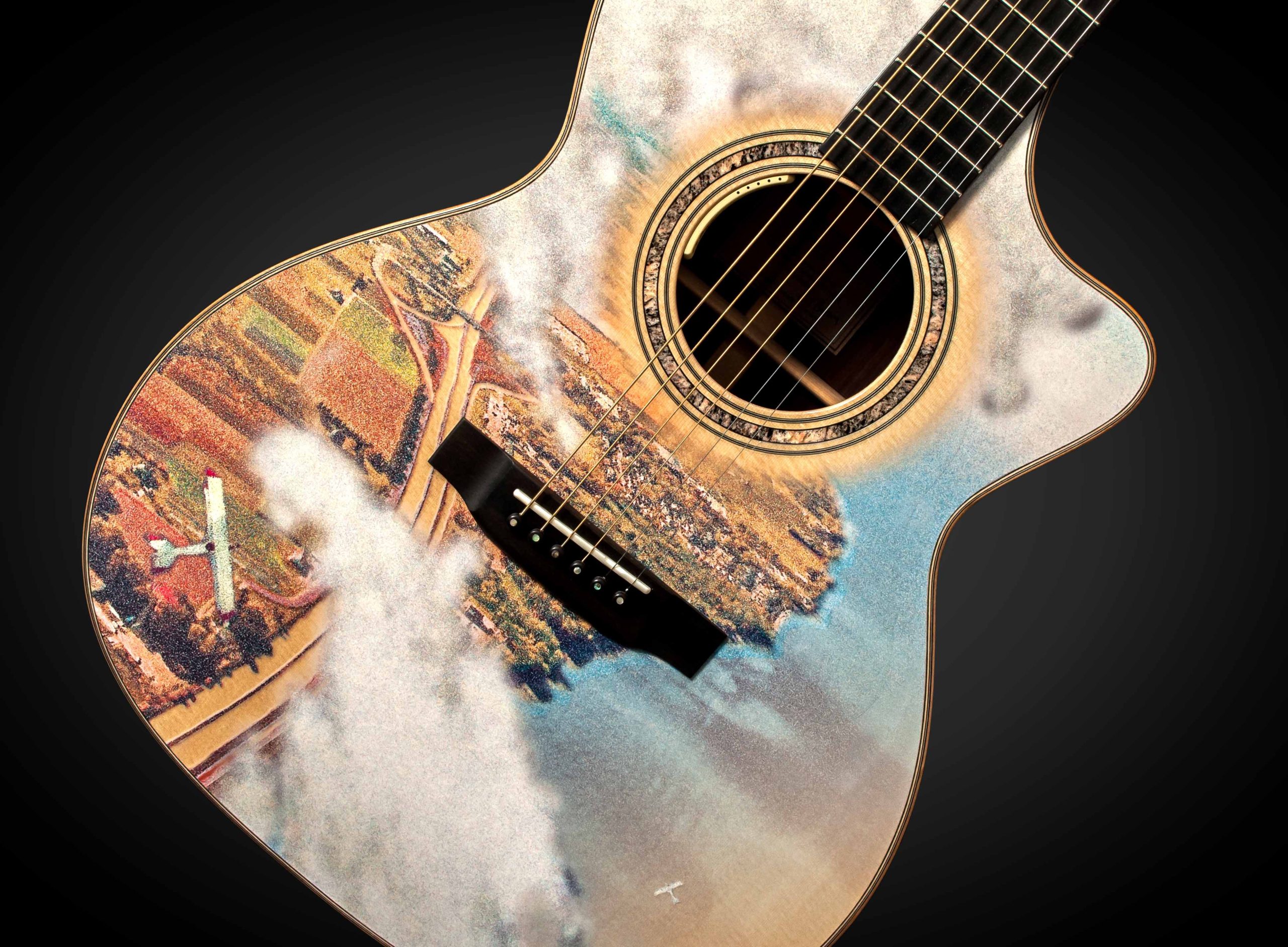 Photograph of the front of a guitar body. The body has an aerial view of a landscape looking down through clouds. There are two small white aeroplanes flying over a patchwork of fields on the left, a highway and a town which borders a shoreline on the right. The body of water is shades of blue.