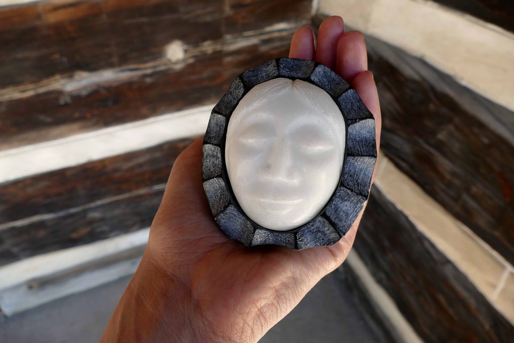 photograph of a hand holding a white stone sculpture of a face with dark grey surround